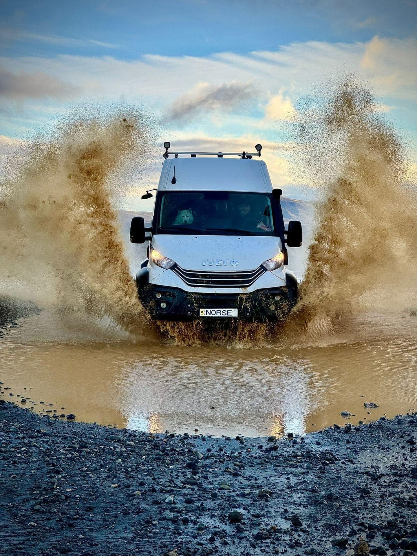 A Floki Whiskey bottle standing on a lava rock in front of an active volcanic eruption